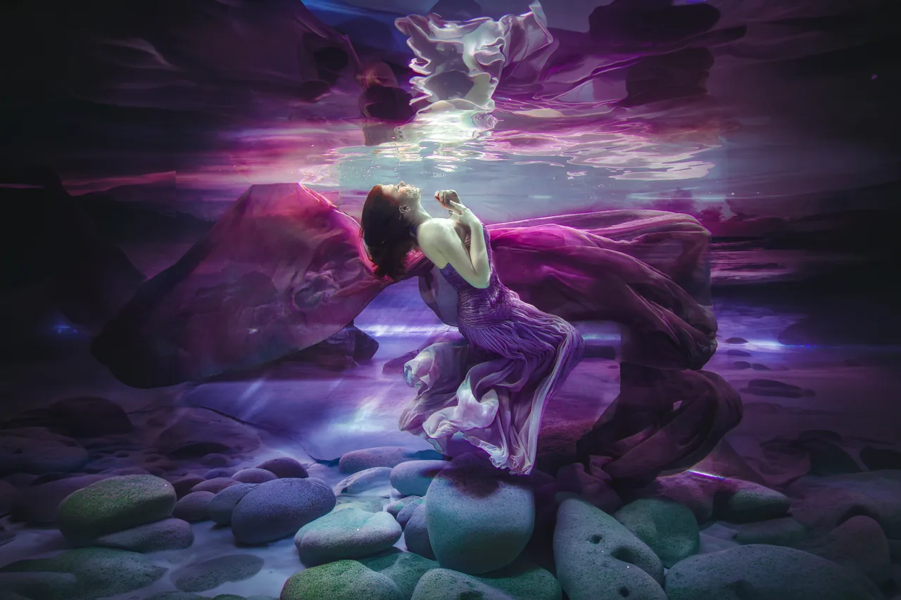 A woman suspended underwater in violet silk, looking up