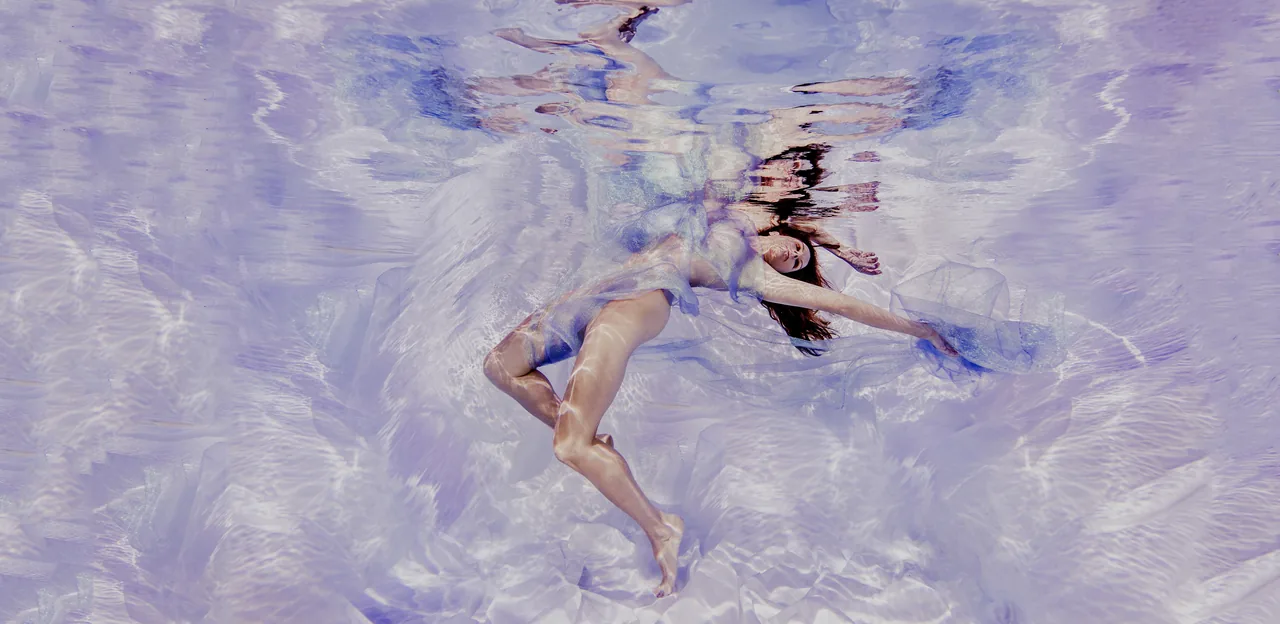 A woman floating in lilac water, seen from below