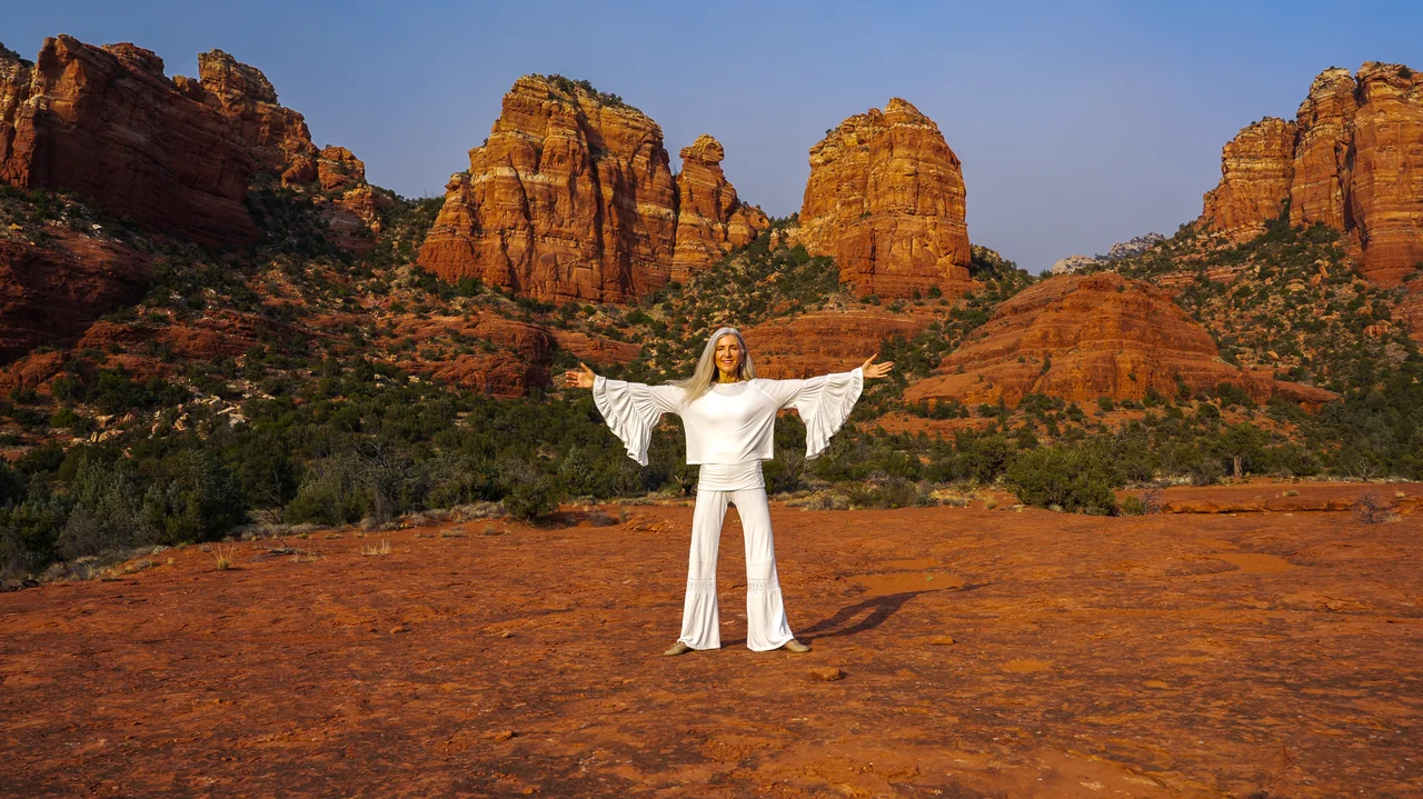 Iana Lahi in white among the red rocks of Sedona, arms outstretched
