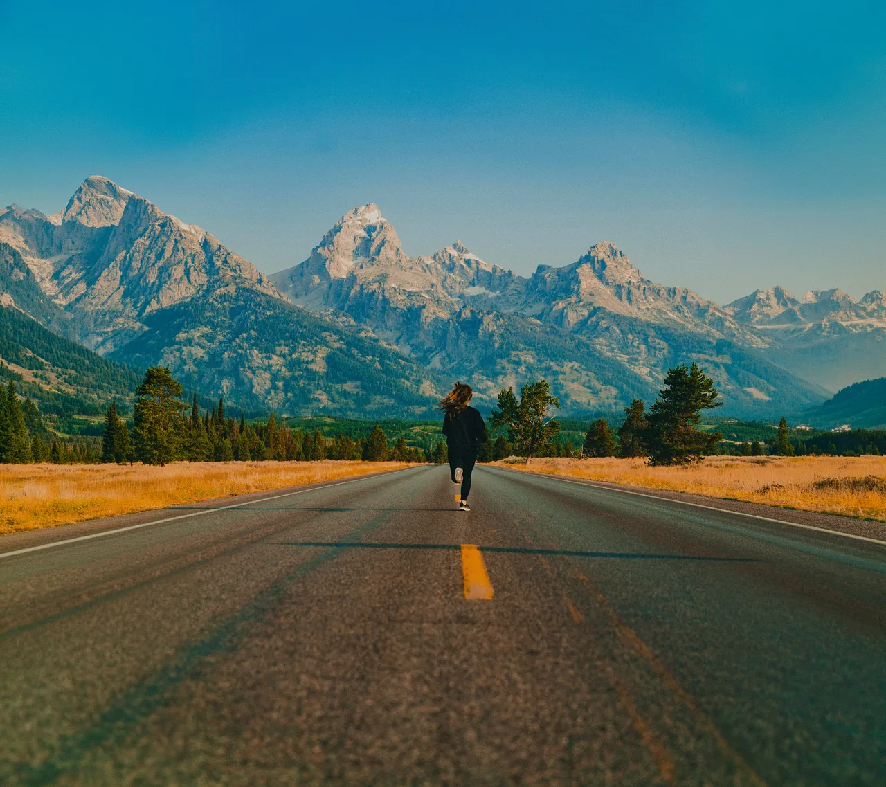 A woman walking a long road toward the mountains