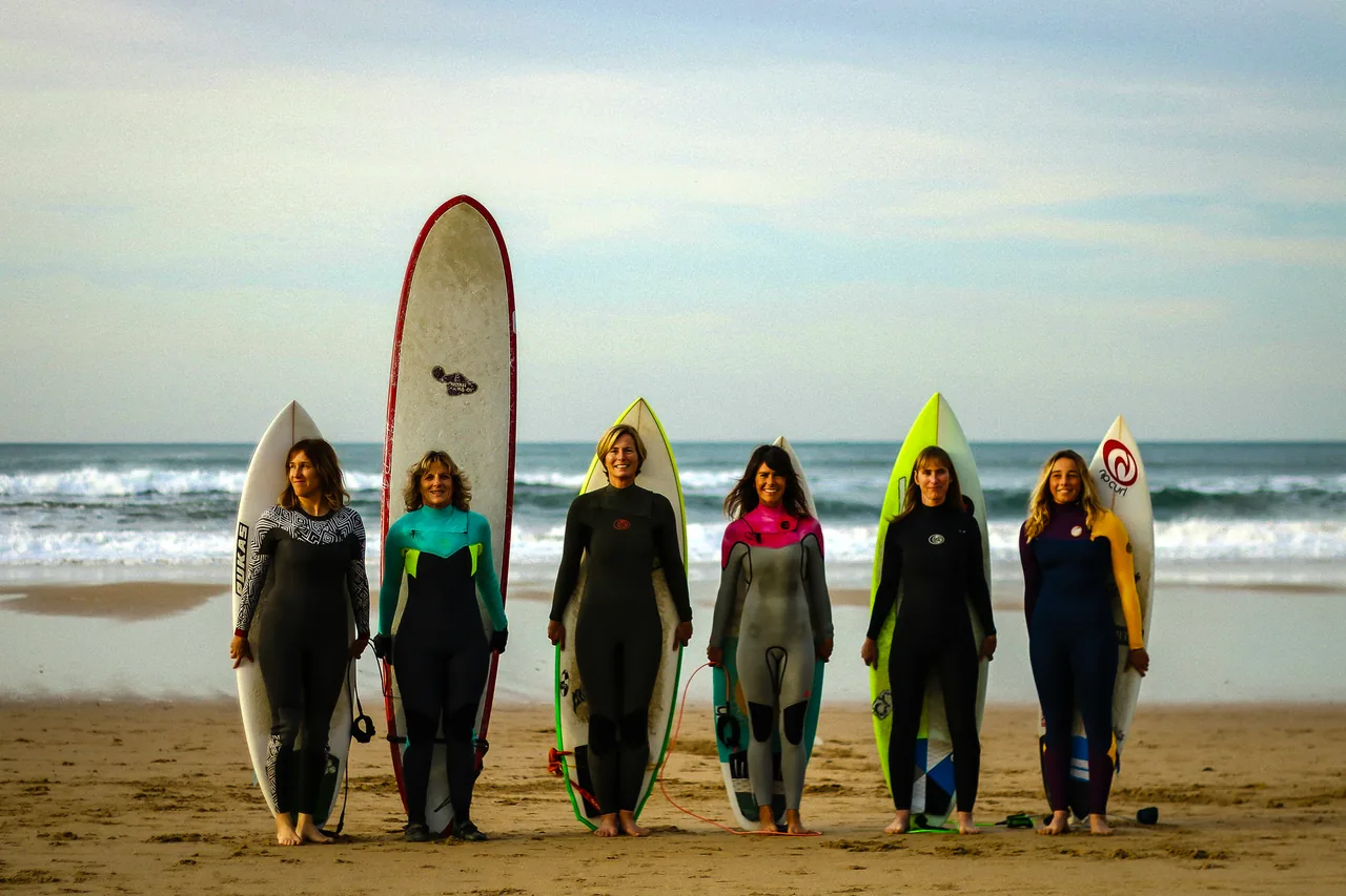 Six women standing with surfboards at the water’s edge