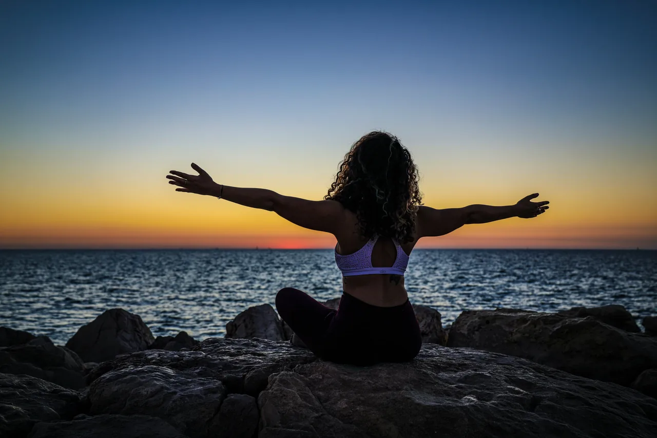 A woman seated by the sea at sunset, arms open